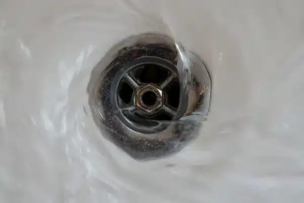 Water swirling down a metal drain in a sink, creating a vortex pattern.