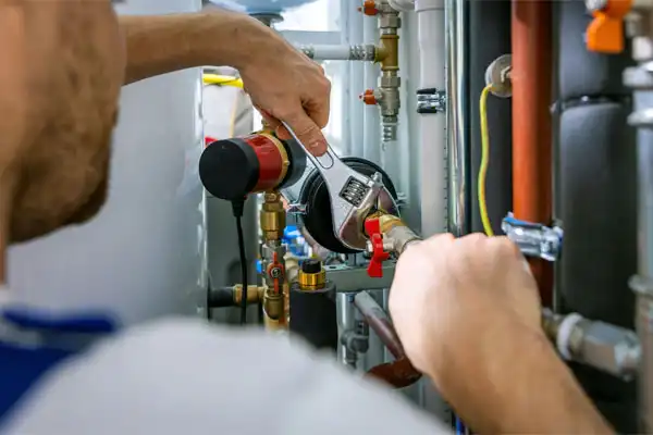Person using a wrench to adjust plumbing valves and pipes in a mechanical room.