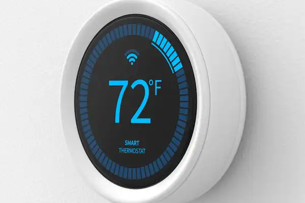 Round smart thermostat on a wall displaying 72°F with a Wi-Fi icon above the temperature and a blue segmented circle indicating settings or connectivity.