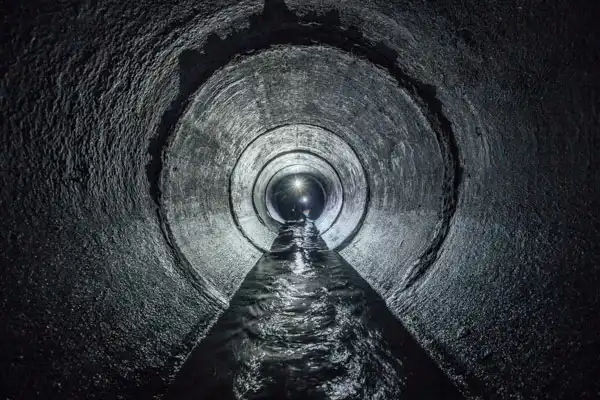 Inside a dimly lit tunnel with dark, textured walls, a narrow stream of water flows along the center.