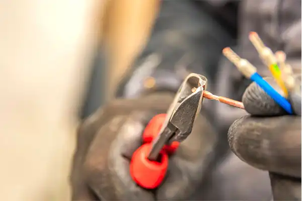 Gloved hands cutting electrical wires with red-handled pliers.