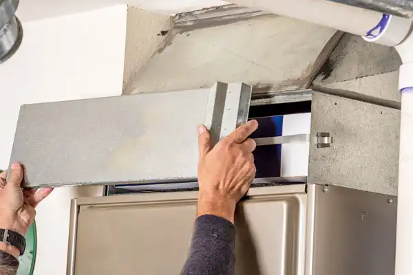 Hands removing an HVAC air filter from a residential furnace unit.