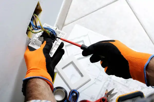 Person wearing orange gloves fixing an electrical outlet with a screwdriver.