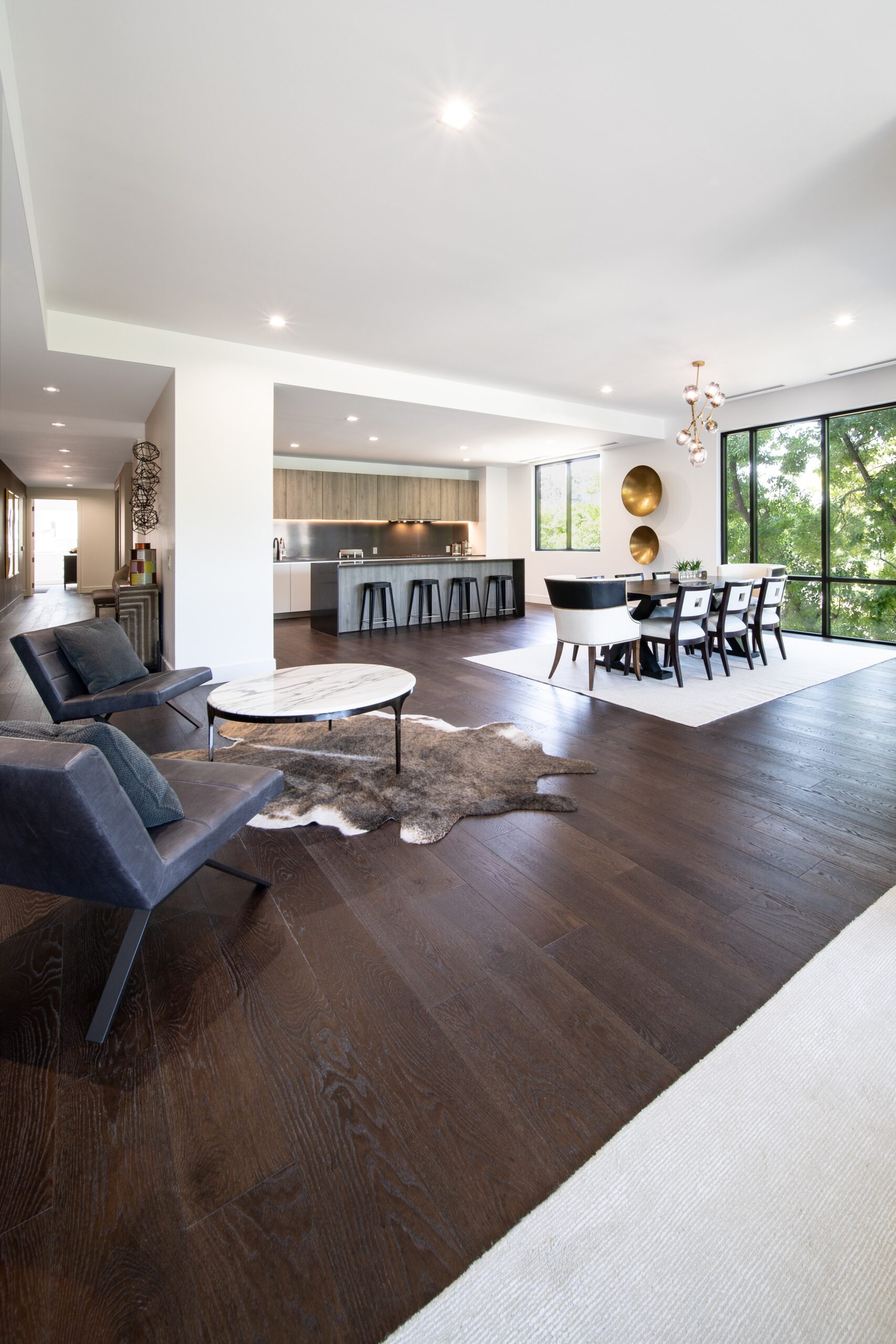 Home Service Blogs | Mighty Plumbing &Amp; Heating Open-Concept Living Area With Dark Wood Floors, A Modern Kitchen, Dining Table, And Lounge Chairs. Large Windows Provide Natural Light And Outdoor Views.