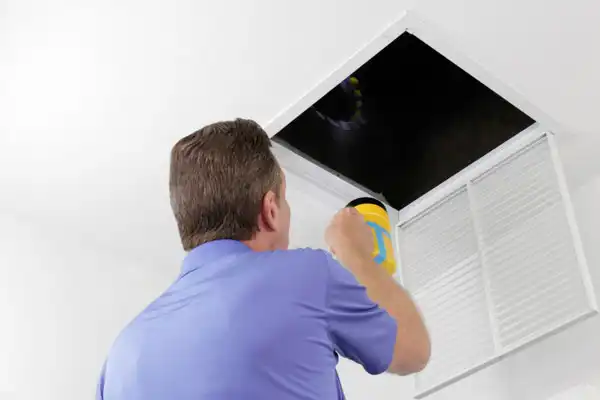 Person shining a flashlight into an open ceiling vent.