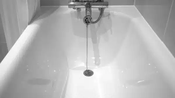 A clean, empty bathtub with a metal chain attached to the drain stopper, located in the center of a tiled bathroom.