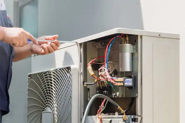 Technician uses a screwdriver to repair an open air conditioning unit showing various wires and components.