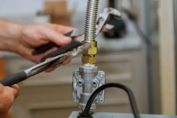 Hands using pliers to tighten a fitting on a metal gas pipe in a domestic setting.