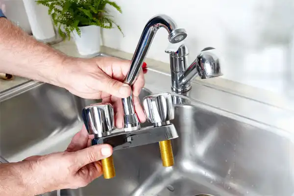 Person holding a detached kitchen faucet above a stainless steel sink, preparing for installation or repair.