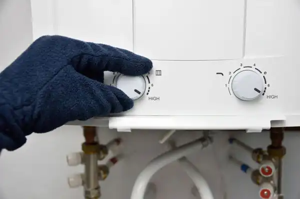 A gloved hand adjusts the temperature dial on a home water heater.