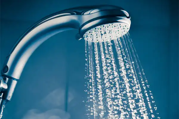 Close-up of a showerhead spraying water droplets against a blue background.