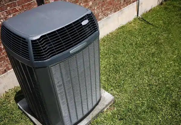 Outdoor air conditioning unit on a concrete slab beside a brick wall and grass lawn.
