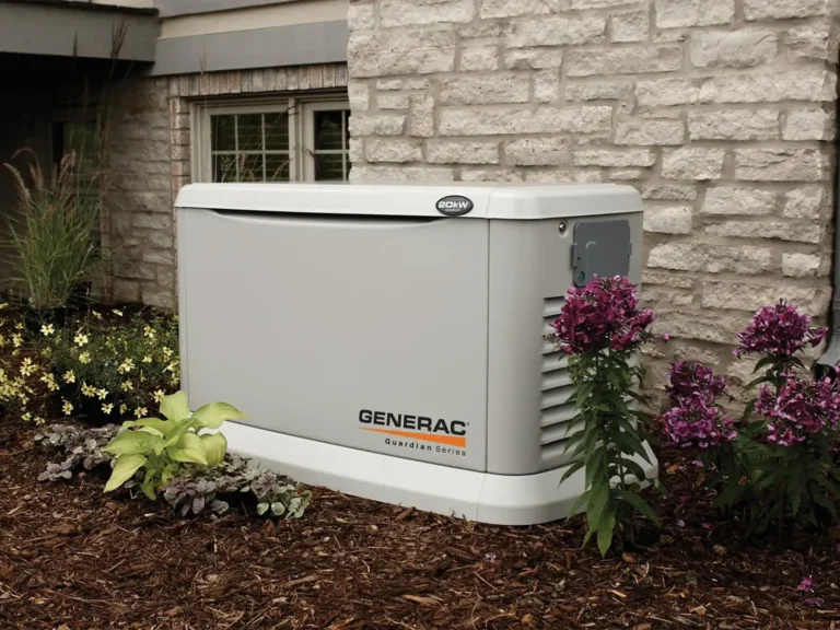 A Generac Guardian Series standby generator is installed outside a house with stone siding, surrounded by mulch, flowers, and plants.